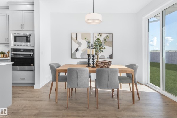 Dining area with a wooden table, grey chairs, and a sliding glass door to the backyard. - 1424 Cristall Pl Sw, Edmonton