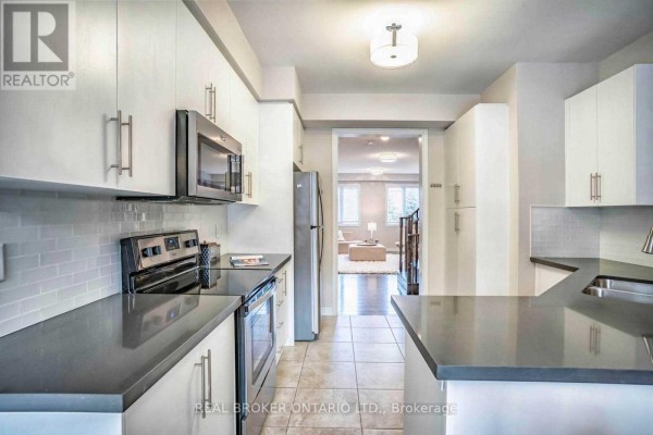 Kitchen with white cabinetry, stainless steel appliances, and a view into the living area. - 1424 Granrock Crescent, Mississauga