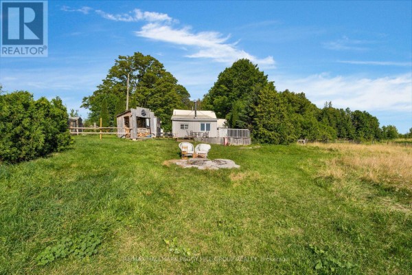 View of a small grey building with two white chairs and a fire pit in the yard. - 1424 Klondike Park Road, Clearview