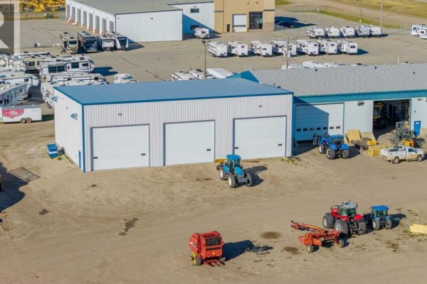 Side view of the commercial building with three white garage doors and a tractor. - 14250 100 Street, Rural Grande Prairie No  1, County Of
