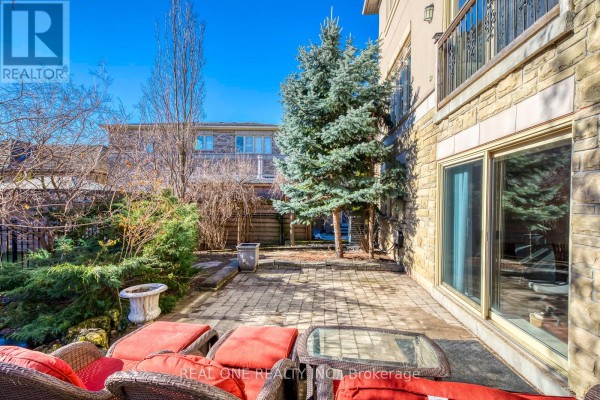 Paved backyard patio with wicker furniture and glass table next to stone home - 1426 Redwing Court Oakville