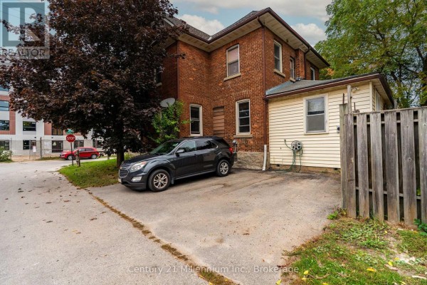 Backyard view of the brick house with a driveway, a dark SUV, and a wooden fence. - 143 11th Street W, Owen Sound