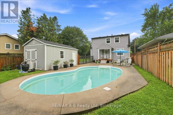 Backyard with a kidney-shaped pool, concrete patio, and wooden fence. - 143 Britannia Street, Stratford