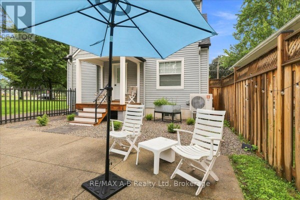 Patio with blue umbrella, white chairs, and a wooden fence - 143 Britannia Street Stratford