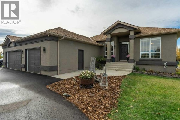 Front exterior of a stucco house with a gray trim, covered entrance, and a three-car garage. - 143 Crocus Ridge Drive, Rural Rocky View County