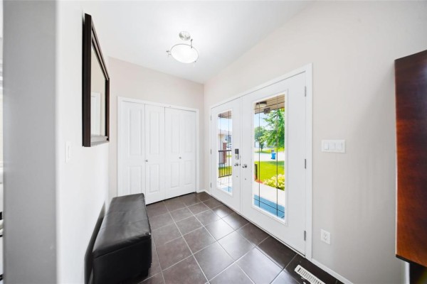 Interior foyer with tiled floor, double entry doors, and a black bench against a wall. - 143 Mosselle Drive, Winnipeg