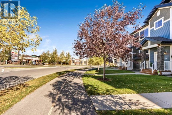 Street view of a townhouse complex with trees and a sidewalk. - 143 Nolan Hill Boulevard Nw, Calgary