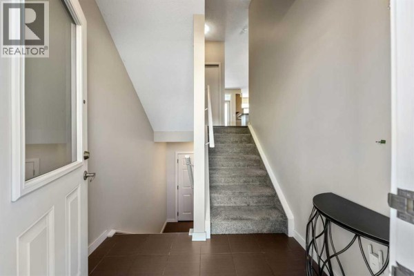 Interior view of a townhouse entrance with a staircase and dark tiled floor. - 143 Nolan Hill Boulevard Nw, Calgary