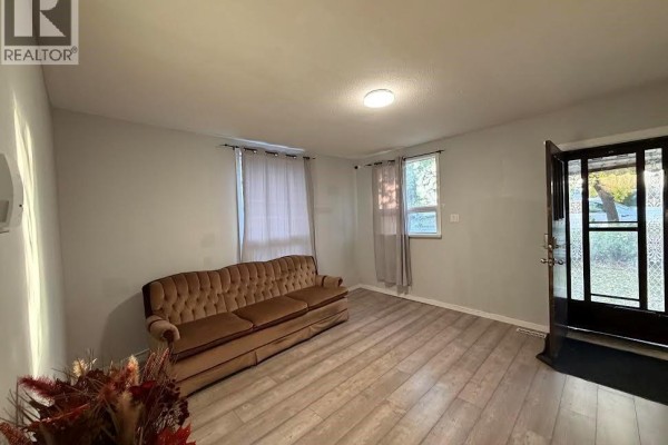Living room with a brown tufted sofa, light grey walls, and light wood laminate flooring. - 143 Sixth Avenue N, Yorkton