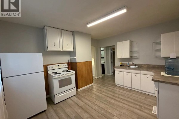 Kitchen with white appliances, white cabinetry, and light wood laminate flooring. - 143 Sixth Avenue N, Yorkton