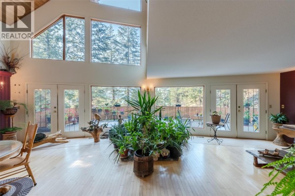 Spacious living area with floor-to-ceiling windows, numerous plants, and access to a deck. - 143 Stage Coach Road, Keremeos