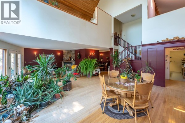 Great room with a stone fireplace, staircase, dining table, and abundant houseplants. - 143 Stage Coach Road, Keremeos