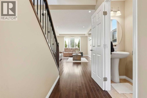 Hallway view showing dark wood floors, staircase, and doorway to a living area and powder room. - 143 Windbrook Manor Sw, Airdrie