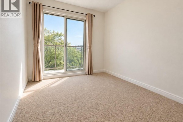 Bedroom with a metal frame bed, beige carpet, and sliding glass door with balcony view. - 1430 Highland Road W Unit# 36b, Kitchener