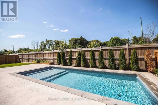 Backyard with a rectangular swimming pool, concrete patio, wooden fence, and green landscaping. - 1430 Simpkin Road, Innisfil
