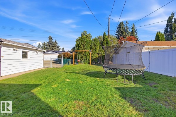 View of the backyard with a trampoline, swing set, garage, and white vinyl fencing. - 14312 89a Av Nw, Edmonton