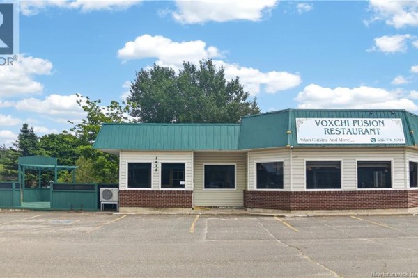 Rear side of the commercial building, showing white siding, windows, and a grass area. - 1434 Principale, Neguac