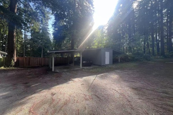 Carport with attached shed next to a wooden fence in a forested area. - 14340 28 Avenue, Surrey