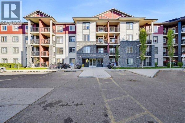 Exterior view of a multi-story apartment building with balconies, red and beige siding, and a paved parking lot. - 1438, 81 Legacy Boulevard Se, Calgary