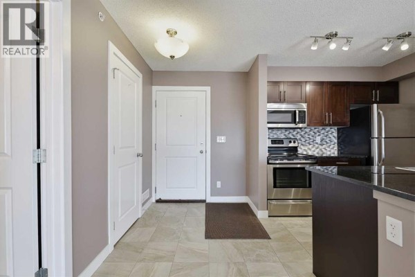 Interior view of an apartment entryway and kitchen with stainless steel appliances and dark wood cabinets. - 1438, 81 Legacy Boulevard Se, Calgary