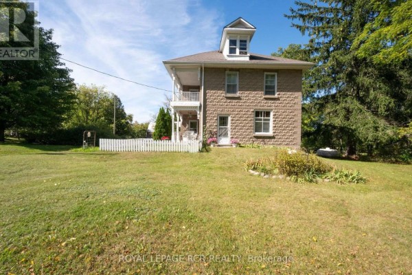 Side view of a stone house with a white picket fence and a large green lawn. - 1438 Concession 3 Road, Adjala Tosorontio