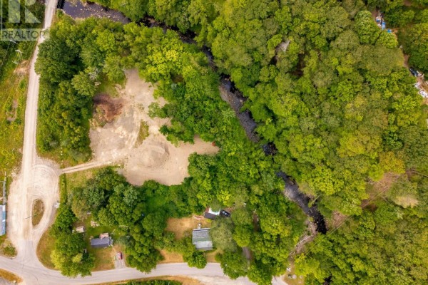 Aerial view shows a cleared section of land next to a winding creek and surrounded by lush green forest. - 1438 River Road, Bear River