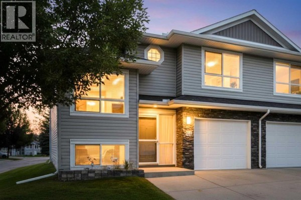 Exterior front view of a duplex at dusk with interior lights on. - 144, 55 Fairways Drive Nw, Airdrie