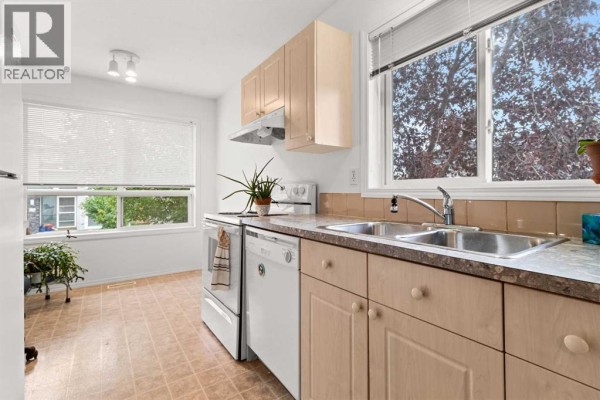 Kitchen counter with a double sink, faucet, and dishwasher, looking out a window. - 144, 55 Fairways Drive Nw, Airdrie
