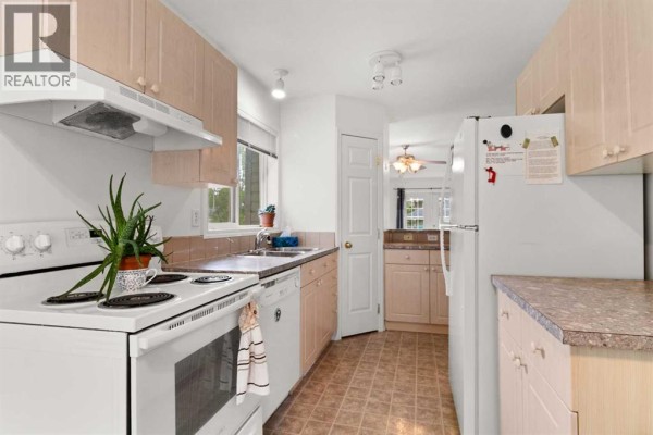 Kitchen area with white appliances, wood cabinetry, and a doorway leading to another room. - 144, 55 Fairways Drive Nw, Airdrie