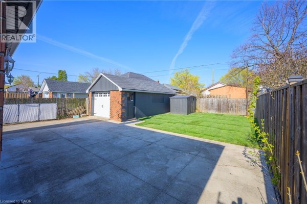 Backyard with a concrete driveway, a detached garage with a white door, and a small grassy area. - 144 East 44th Street Unit# Lower Unit, Hamilton