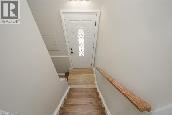 View looking down a staircase with wooden steps, a white door at the bottom, and light grey walls. - 144 East 44th Street Unit# Lower Unit, Hamilton