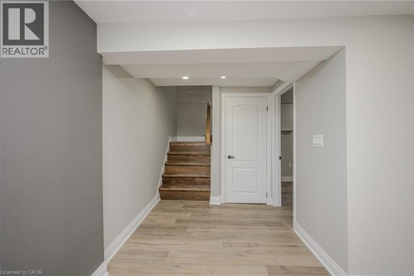 Interior view of a hallway with light grey walls, wooden floors, stairs, and two white doors. - 144 East 44th Street Unit# Lower Unit, Hamilton