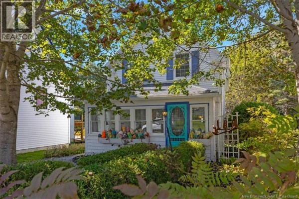 Front view of a quaint white house with a brightly colored door and abundant foliage. - 144 Frederick Street, Saint Andrews