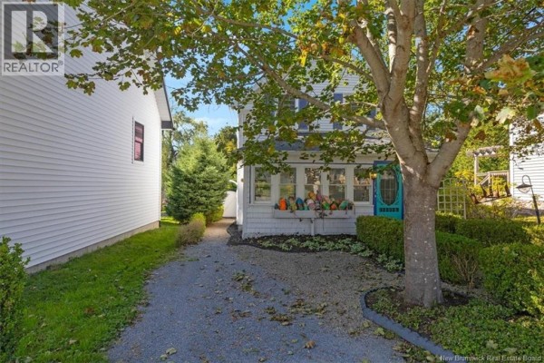 Side view of a white house showing the gravel driveway, surrounding trees, and well-kept landscaping. - 144 Frederick Street, Saint Andrews