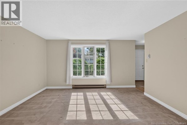 Living room with tan carpet, light beige walls, and a large window with white curtains. - 144 Harvey Road, Riverview