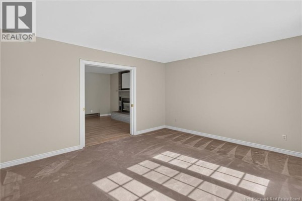 Living room with tan carpet, looking through an open doorway into another room with a fireplace. - 144 Harvey Road, Riverview