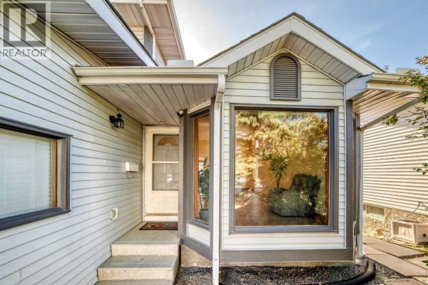 Front entrance of the house with steps, a white door, and a large bay window. - 144 Hawkdale Close Nw, Calgary