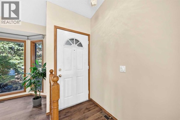 Interior entryway with a white front door, wooden banister, and light beige walls. - 144 Hawkdale Close Nw, Calgary