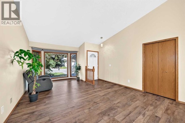 Living room with a bay window, wood laminate flooring, and a bi-fold closet door. - 144 Hawkdale Close Nw, Calgary