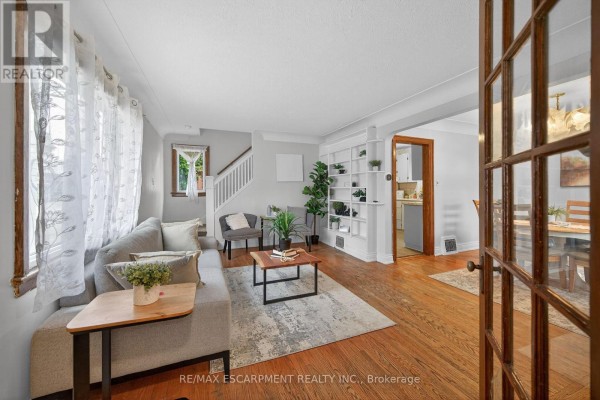 Living room with grey sofa, coffee table, hardwood floors, and a doorway to dining area. - 144 Hunter Street W, Hamilton