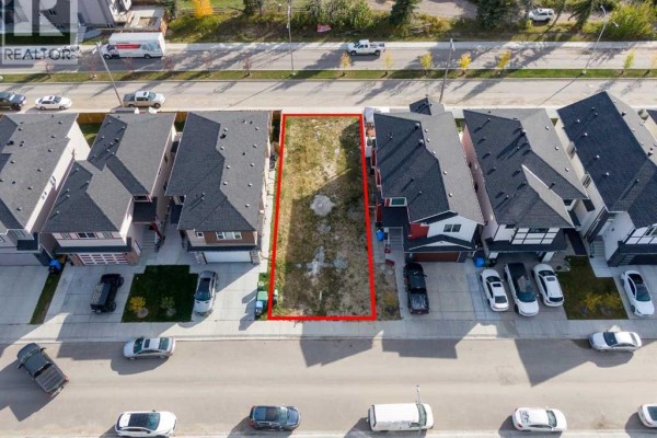 Top-down view of an undeveloped rectangular lot marked with red lines, featuring grass and dirt, between two townhouses. - 144 Saddlecrest Circle Ne, Calgary