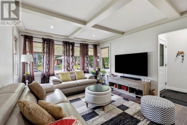 Living room with beige sectional sofa, two armchairs, coffered ceiling, and large television. - 144 Shannon Rd, Sault Ste  Marie