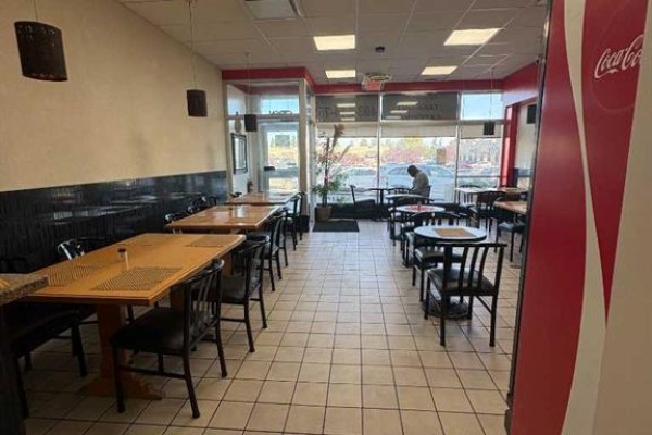 Interior of a restaurant with tables and chairs, tiled floor, and large windows. - 1440 52 St  Ne, Calgary