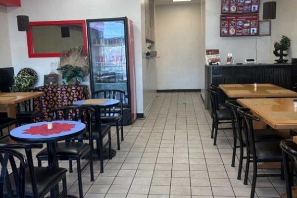 Interior of a restaurant showing dining tables, chairs, a beverage cooler, and a service counter. - 1440 52 St  Ne, Calgary
