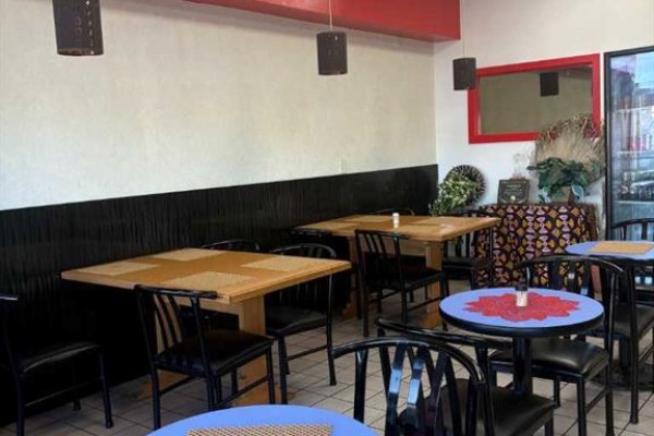 Restaurant dining area with wooden tables, black chairs, and a blue decorative table. - 1440 52 St  Ne, Calgary