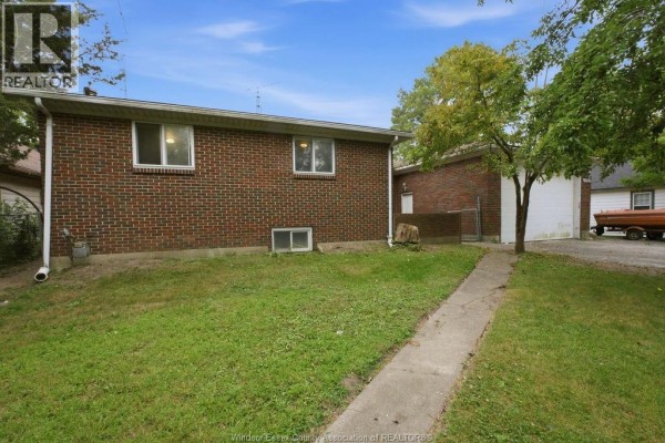 Side view of a brick house with a grassy yard and a concrete path. - 1441 Heritage Road, Kingsville