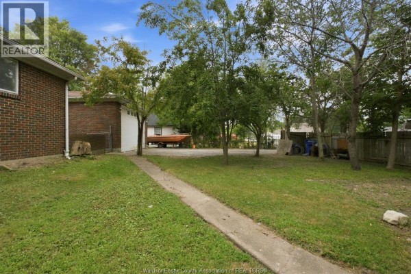 Backyard view of a brick house with a lawn, trees, and a concrete pathway. - 1441 Heritage Road, Kingsville