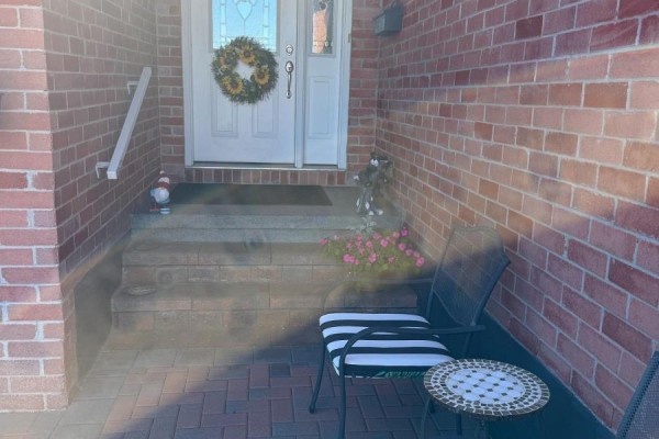 Front porch with brick steps, a white door with a wreath, and a metal chair. - 1442 Windsor Drive, Brockville