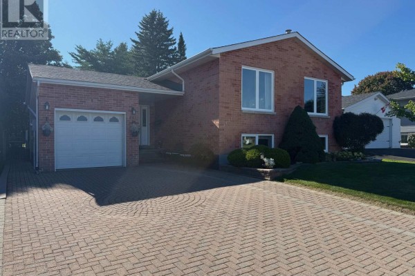Front view of a red brick house with a single car garage and a wide paved driveway. - 1442 Windsor Drive, Brockville