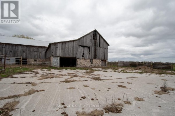 Exterior of a weathered wooden barn with a concrete pad and stone foundation. - 1444 5th Line, Selwyn